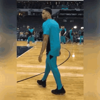 a man in a blue shirt is walking on a basketball court .