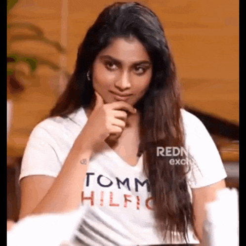 a woman wearing a white tommy hilfiger t-shirt is sitting at a table .