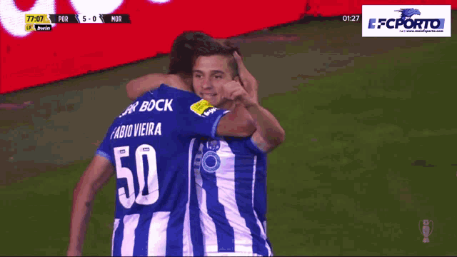 two soccer players are hugging each other on a field with a fc porto banner in the background
