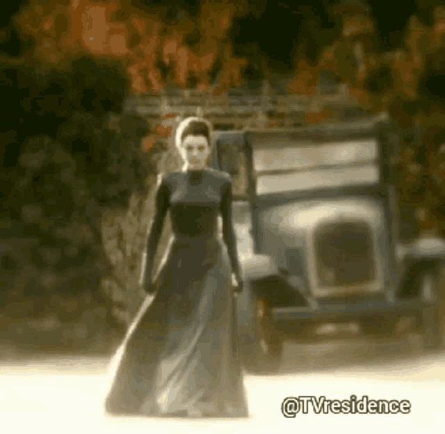 a woman in a long dress is standing in front of a car .