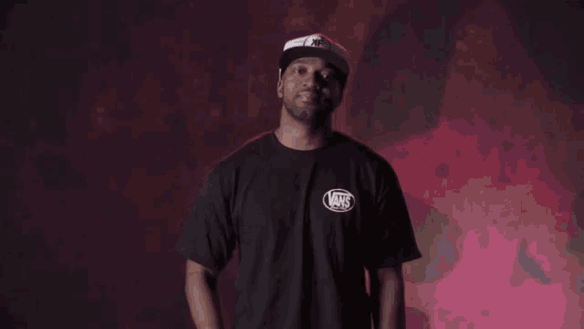 a man wearing a black t-shirt and a white hat is standing in front of a red wall .