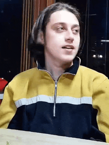 a young man is sitting at a table wearing a yellow and black sweater .
