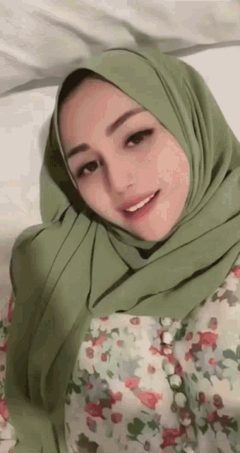 a woman wearing a hijab and a floral shirt is laying on a bed .