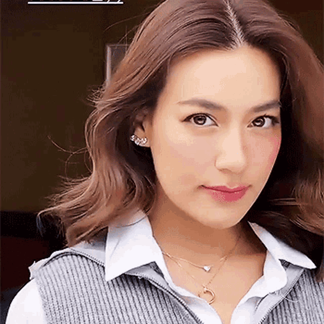 a close up of a woman wearing a sweater vest and a necklace