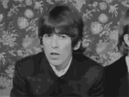 a black and white photo of a man sitting in front of a floral wallpaper .