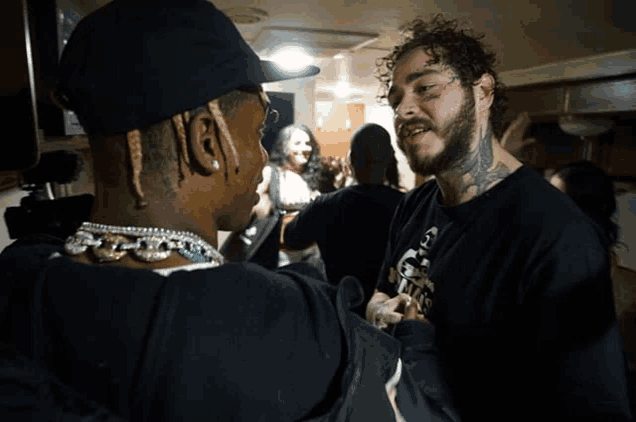 a man with a tattoo on his face talks to another man in a black shirt