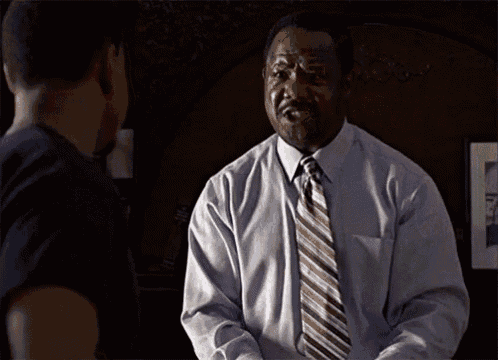 a man in a blue shirt and tie is talking to another man in a black shirt with the word si on it