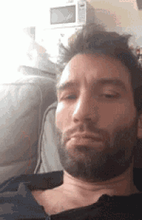a man with a beard is laying on a couch with his eyes closed and making a funny face .