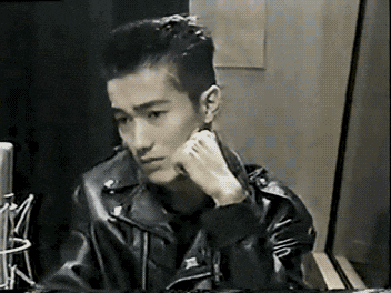 a young man in a leather jacket is sitting at a table with his hand on his chin .