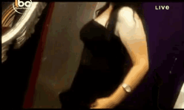 a woman in a black dress is standing in front of a mirror with the word live on the bottom right