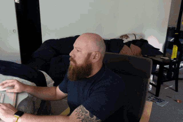 a bald man with a beard is sitting in a chair in a living room