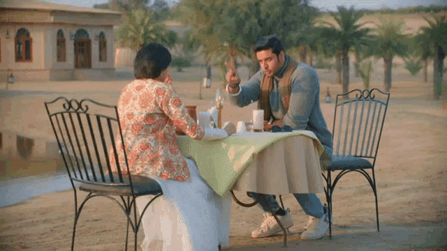 a man and a woman are sitting at a table in the sand