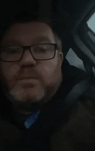a man with glasses and a beard looks at the camera
