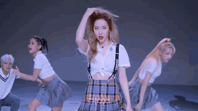 a woman in a plaid skirt and suspenders is dancing with a group of dancers .