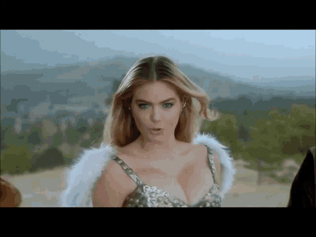 a woman in a silver dress and white wings is standing in front of a mountain .