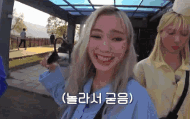 a girl with blonde hair and pink cheeks is smiling and holding a cell phone