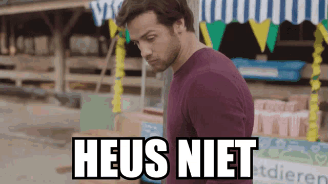 a man in a purple sweater stands in front of a sign that says heus niet