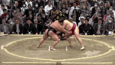 two sumo wrestlers are fighting in a ring with a referee watching