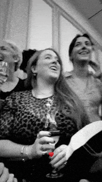 a group of women are sitting next to each other holding glasses of wine and laughing .