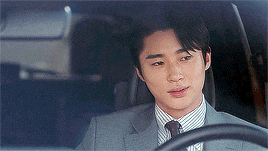 a young man in a suit and tie is driving a car .