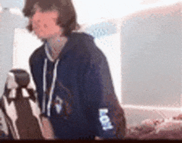 a young man in a blue hoodie is standing next to a stuffed animal .