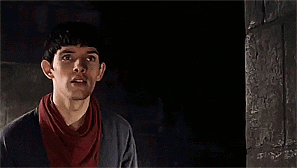 a man with a scarf around his neck is standing in a dark room looking up .