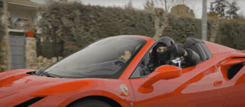 a man wearing a black mask is driving a red sports car