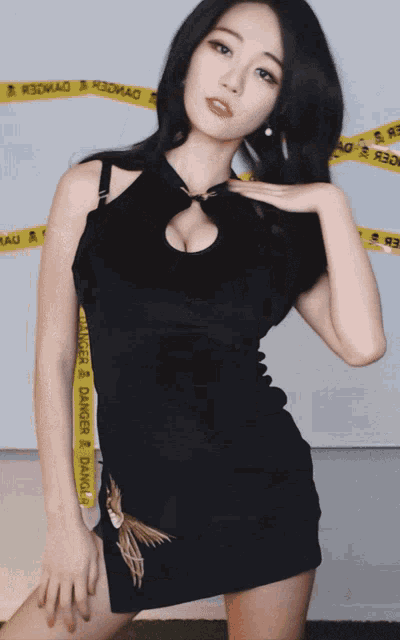 a woman in a black dress is standing in front of a wall with a yellow tape that says ' r3omag '