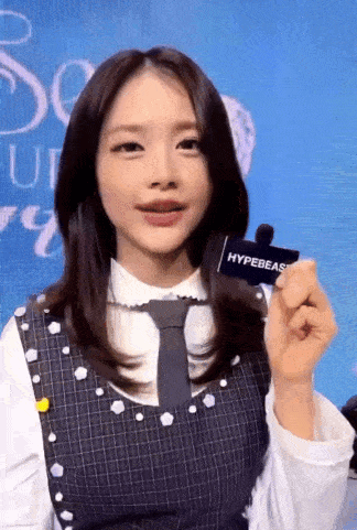 a woman in a plaid dress and tie is holding a hypebeast sticker