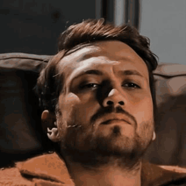 a man with a beard is laying on a couch with his eyes closed and looking at the camera .