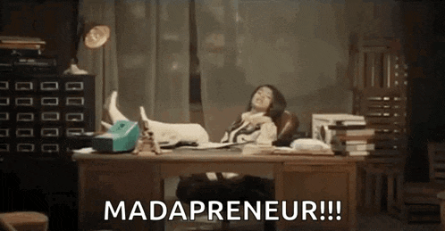 a woman is sitting at a desk with her feet up and the words `` mad entrepreneur '' written above her .