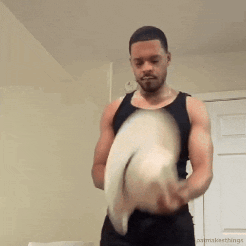 a man in a tank top is holding a cowboy hat in his hands .