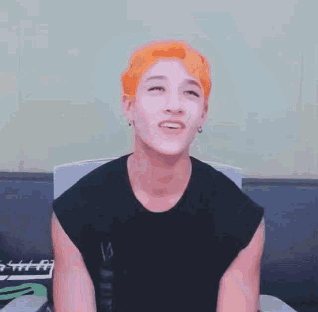 a man with orange hair is sitting on a couch with his eyes closed and his arms in the air .