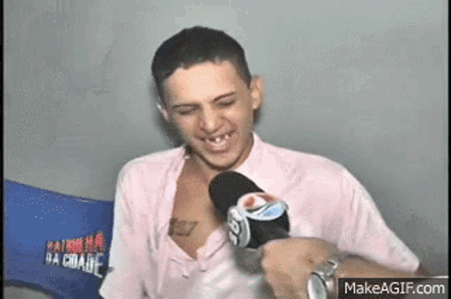 a man with a tattoo on his chest is talking into a microphone while wearing a pink shirt .