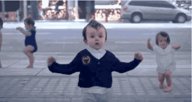 a group of babies are dancing on a sidewalk with one wearing a gucci sweater