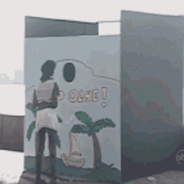 a woman is standing in front of a wall with a painting of palm trees and a sailboat on it .