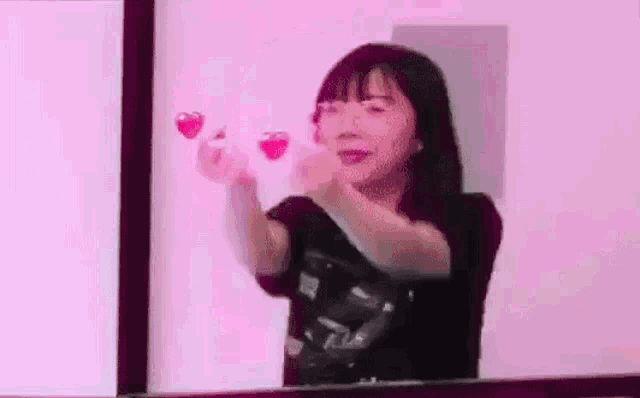 a woman is holding two hearts in her hands in front of a pink background .