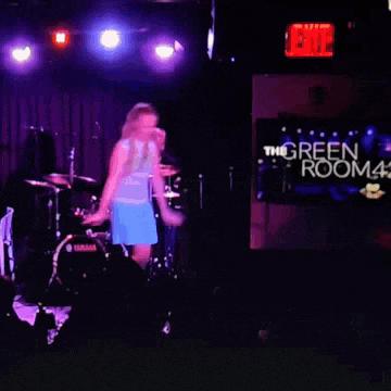 a woman is dancing on stage in front of a sign that says the green room