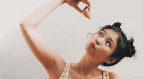 a woman is holding a strawberry in front of her eye and looking up