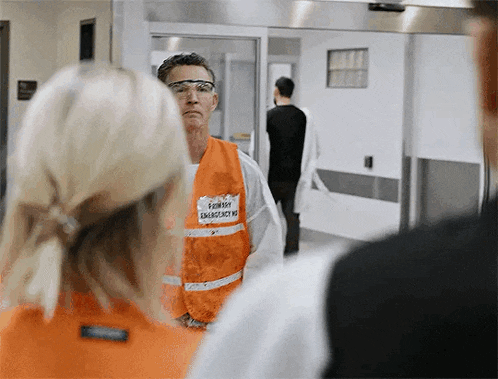 a man wearing an orange vest with the word emergency on it is standing next to a woman .