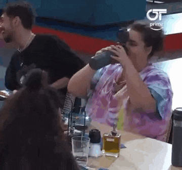 a woman is drinking from a cup while sitting at a table with other people .