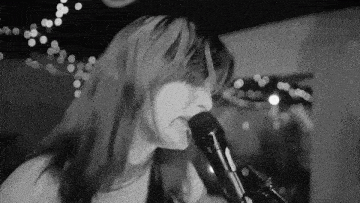 a black and white photo of a woman singing into a microphone in a room .