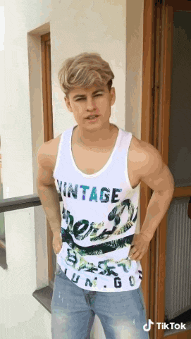 a young man wearing a white tank top with vintage written on it