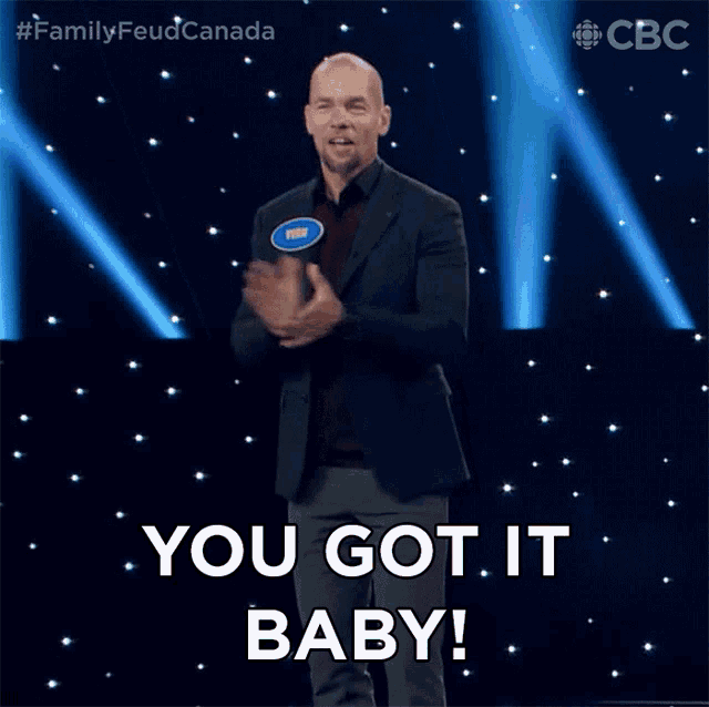 a man in a suit stands on a stage with the words you got it baby behind him