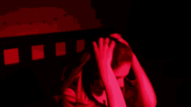 a person covering their face with their hands in a dark room with red lights