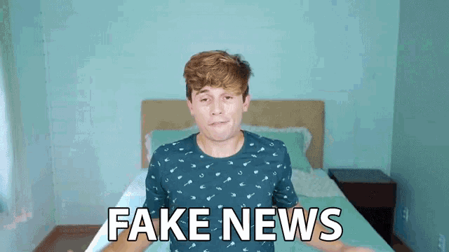 a man in a blue shirt is standing in front of a bed with fake news written on it
