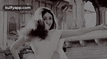 a black and white photo of a woman in a white dress and feathered hat dancing .