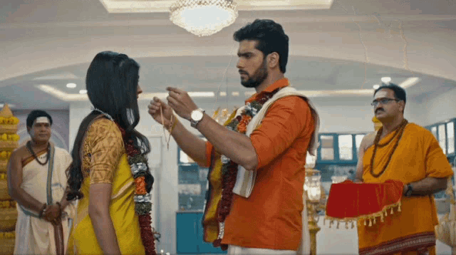 a man in an orange shirt is putting a string around a woman 's wrist