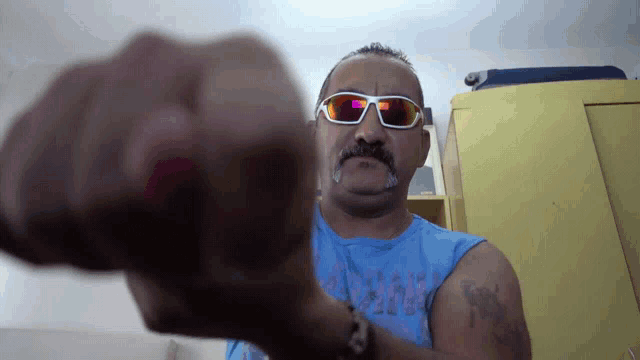 a man wearing sunglasses and a blue shirt has a tattoo on his arm that says ' rock '