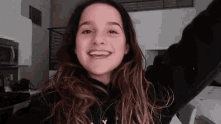 a young girl is taking a selfie with her arms in the air while wearing a black hoodie .